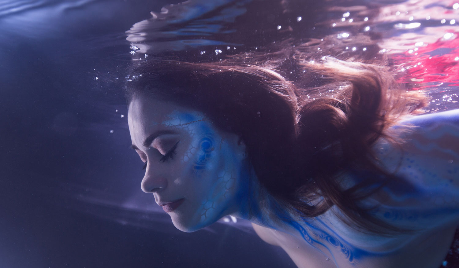 A photo of a woman's head and shoulders submerged in water. Her face and body are painted with scales. The photo was taken as part of a promotion by H&M Communications for the movie the Shape of Water.