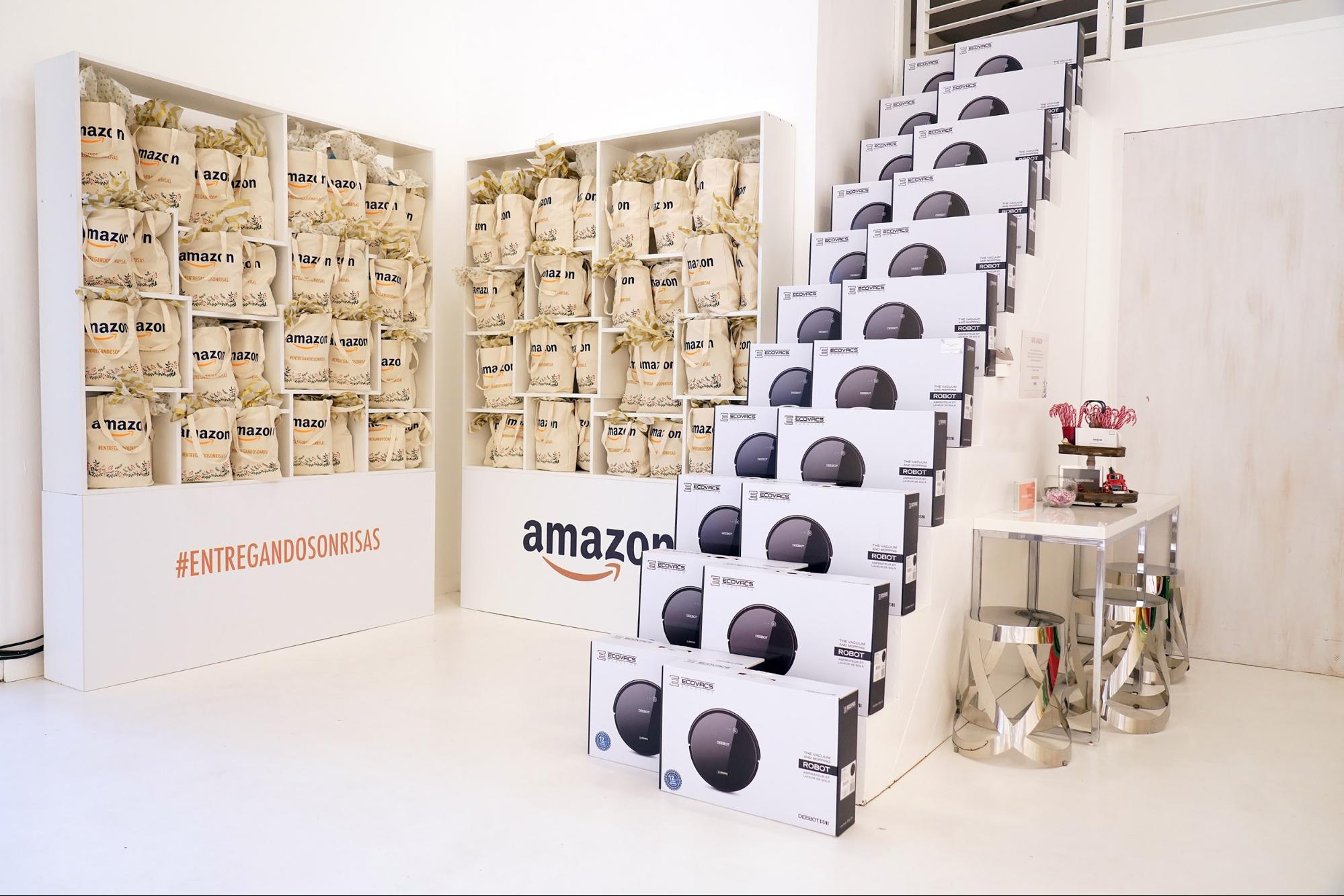 Product boxes for robot vacuums are stacked up white stairs neatly. beside that is a shelf with amazon gift bags and the hashtag #entregandosonrisas