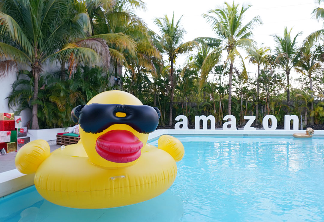 A huge rubber ducky floats in an outdoor pool surrounded by palm trees. The amazon logo is at the end of the pool. The photo was from the Amazon Fiestas event promoted by H&M Communications.